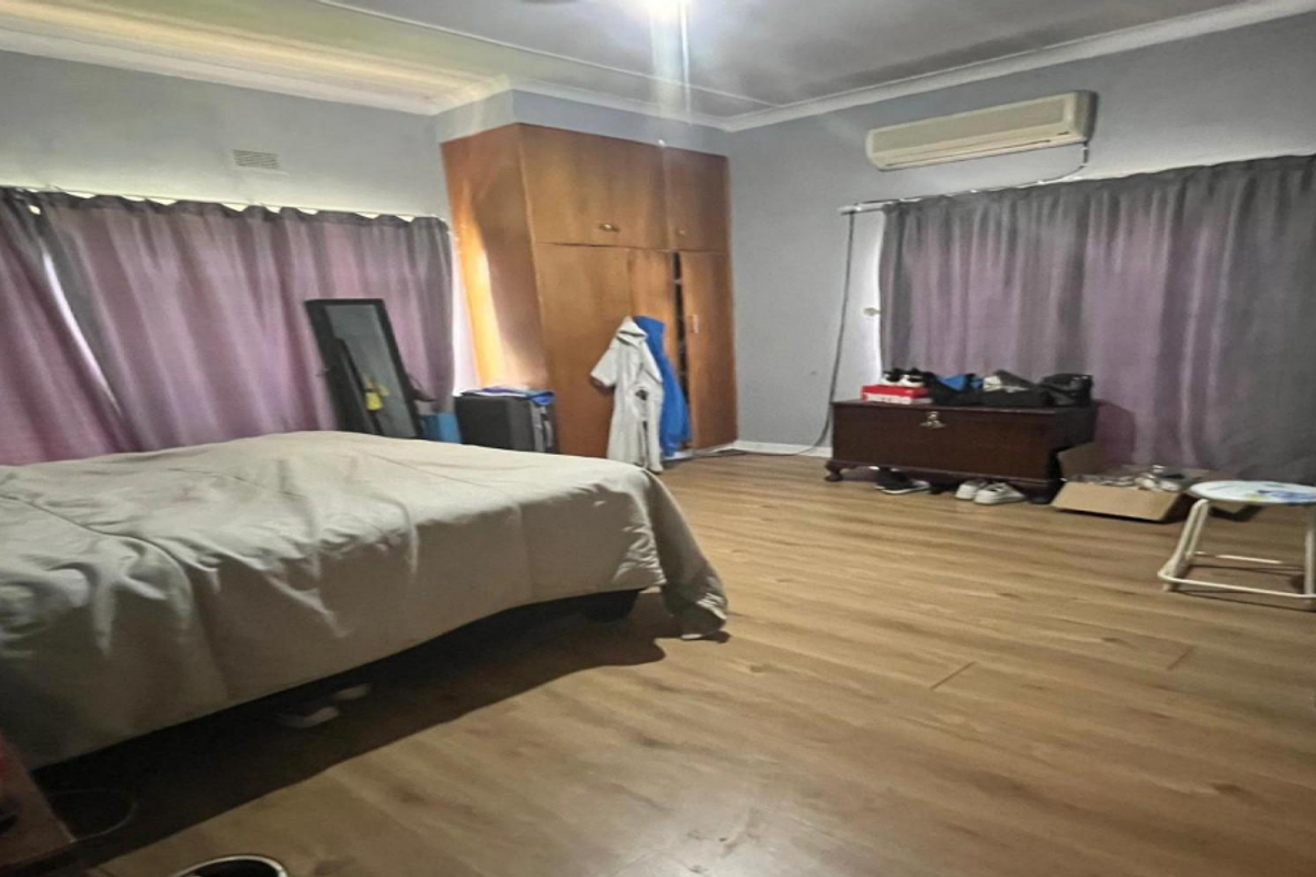 Spacious bedroom featuring laminate flooring, built-in wooden cabinetry, and a wall-mounted air conditioning unit.