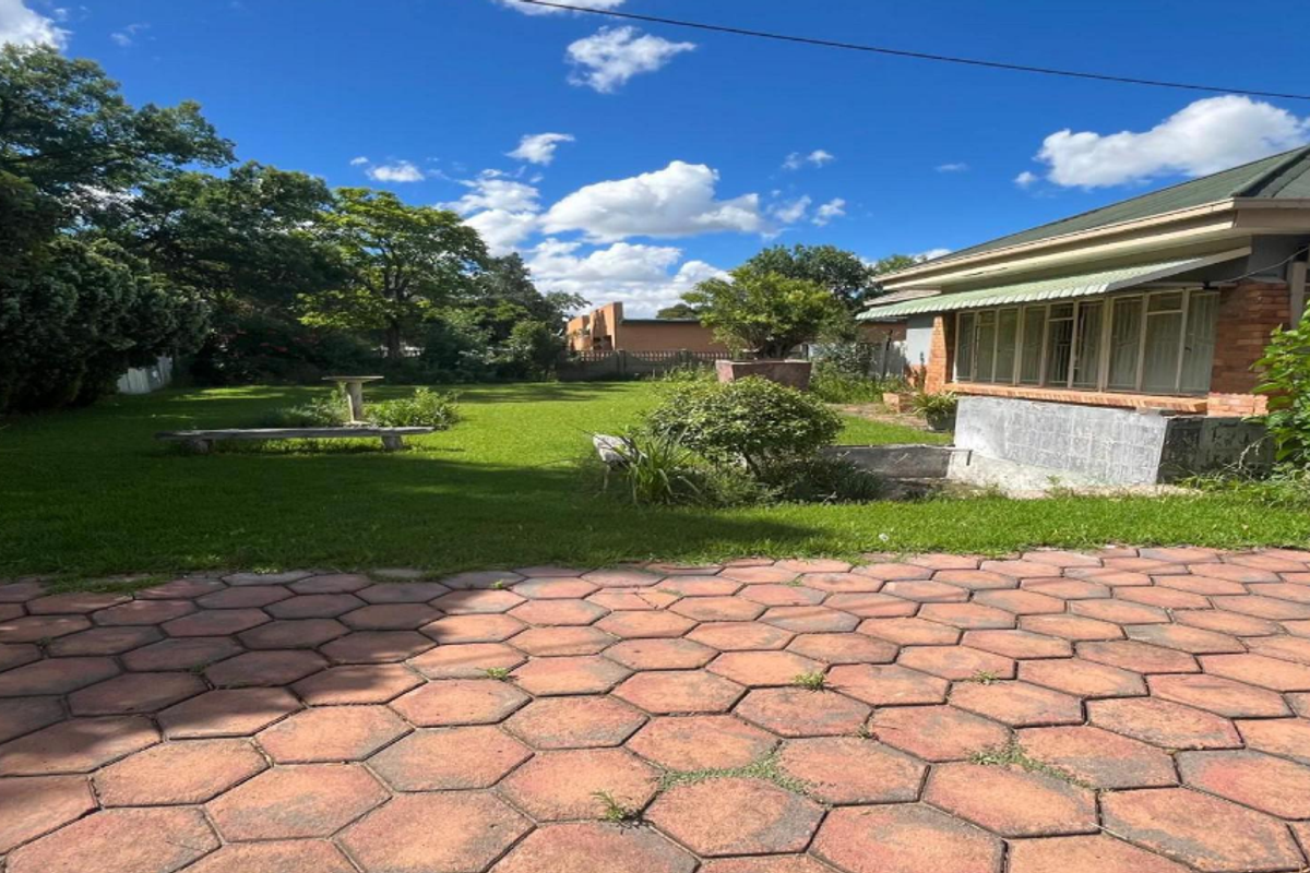 Spacious rear garden featuring a paved patio area, established lawn, and brick exterior facade with metal window frames.