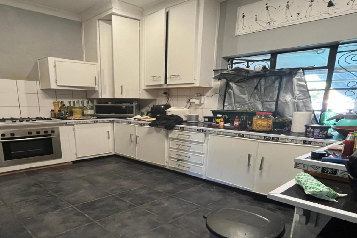 A functional kitchen featuring white cabinetry, a built-in oven, gas hob, and tiled splashbacks, with a window fitted with a security gate.