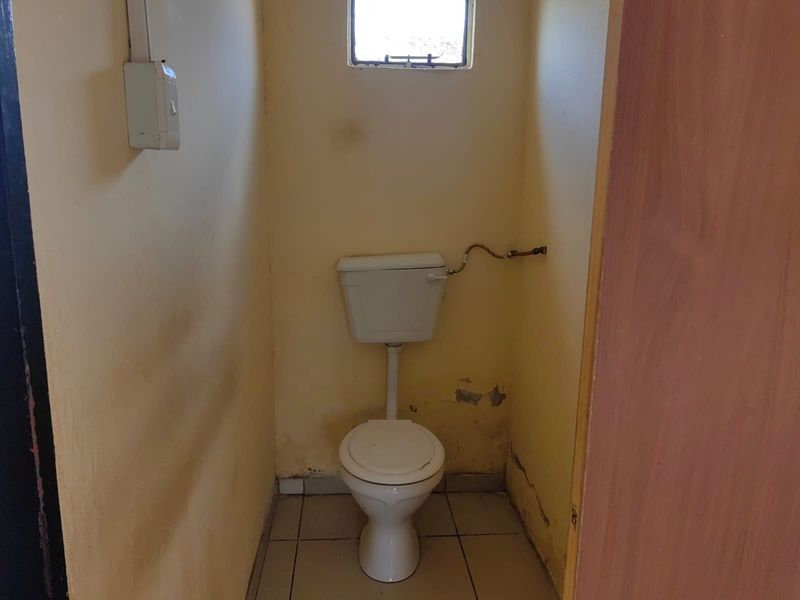 A small, dated bathroom featuring a standard toilet and tiled flooring, currently in need of cosmetic renovation and wall repairs.