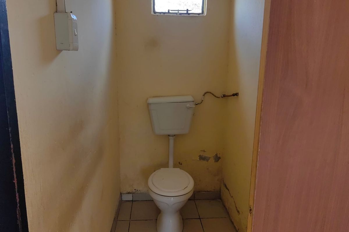 A small, dated bathroom featuring a standard toilet and tiled flooring, currently in need of cosmetic renovation and wall repairs.
