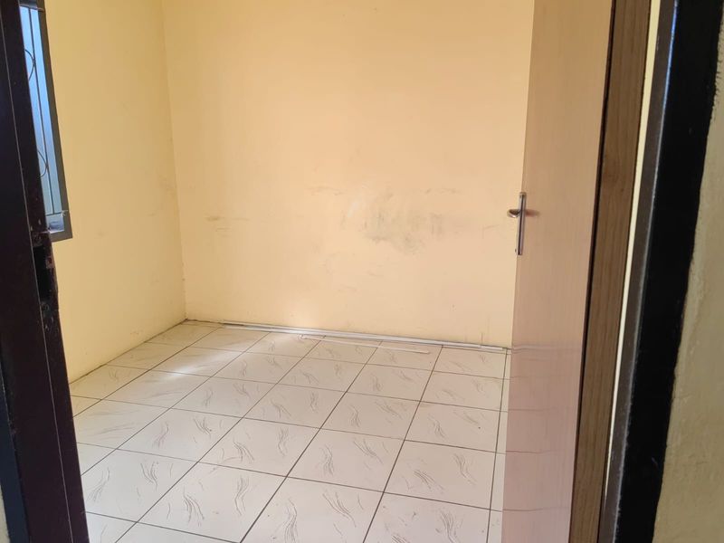An empty bedroom featuring tiled flooring and a window with security bars, requiring minor cosmetic updates to the wall finishes.