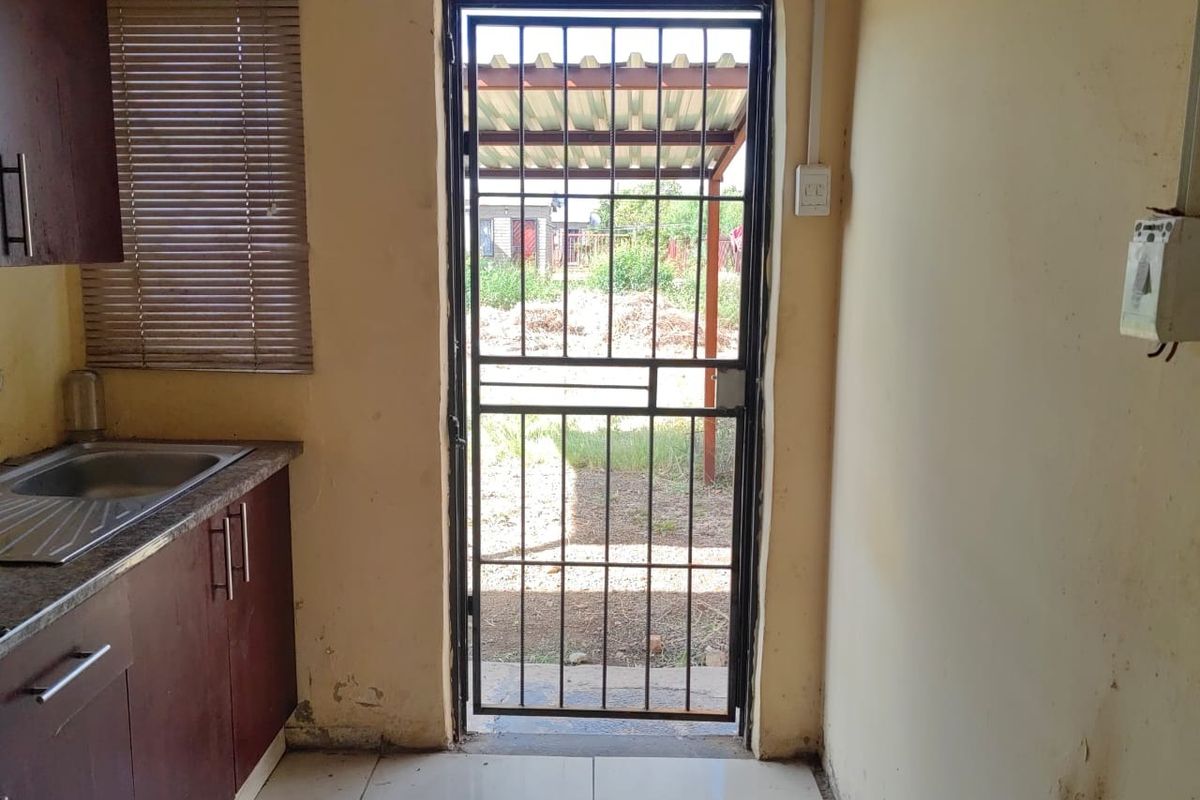 A compact kitchen area featuring built-in cabinetry, a stainless steel sink, and a security gate leading to the exterior.