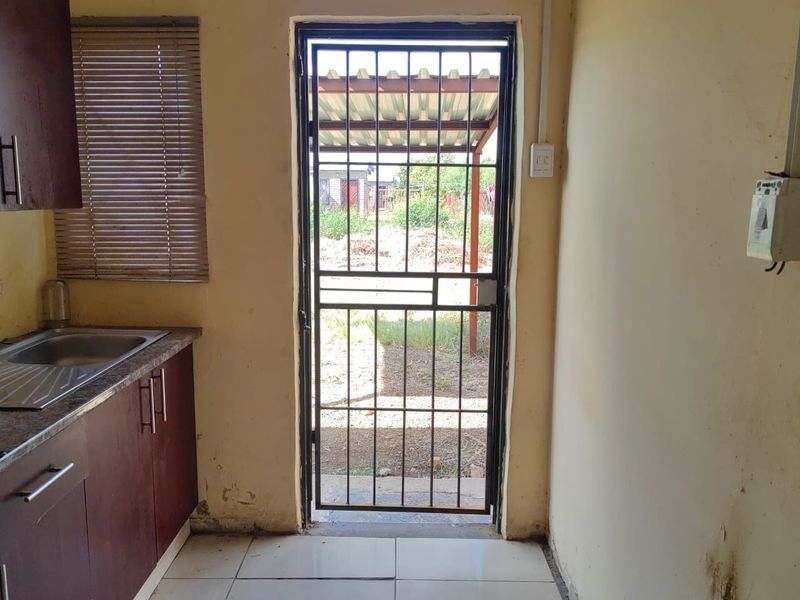 A compact kitchen area featuring built-in cabinetry, a stainless steel sink, and a security gate leading to the exterior.