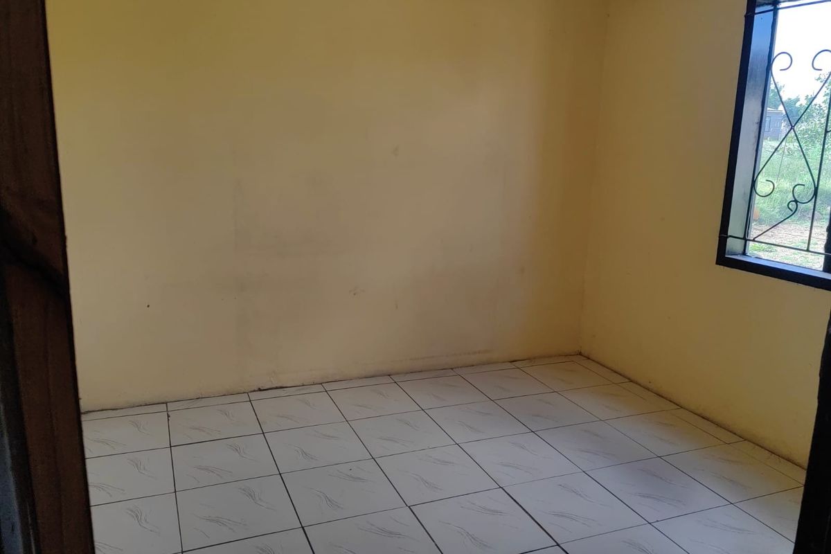 An empty bedroom featuring tiled flooring and a window with a security grille, requiring minor cosmetic updates to the walls.
