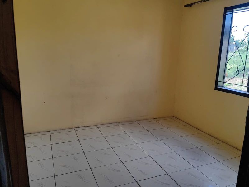 An empty bedroom featuring tiled flooring and a window with a security grille, requiring minor cosmetic updates to the walls.