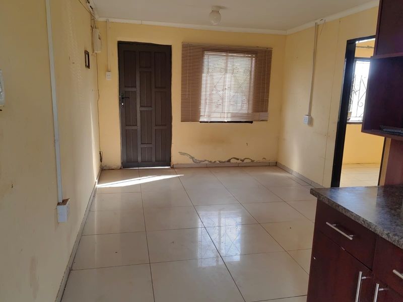 An empty open-plan living and kitchen area featuring tiled floors, built-in cabinetry, and visible wall damage requiring maintenance.