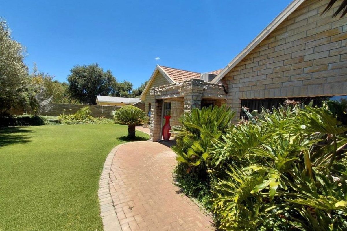 A well-maintained rear garden featuring a brick paved walkway, stone-clad exterior wall details, and a lush lawn area.