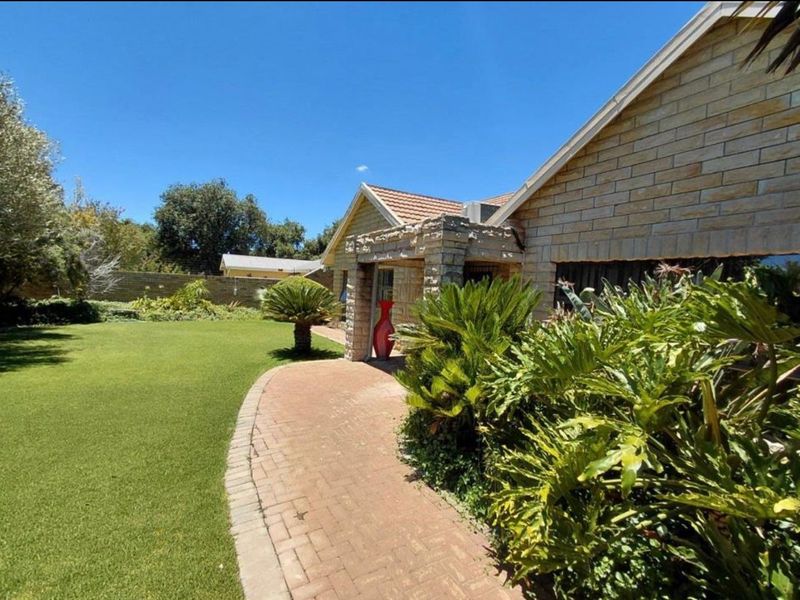 A well-maintained rear garden featuring a brick paved walkway, stone-clad exterior wall details, and a lush lawn area.