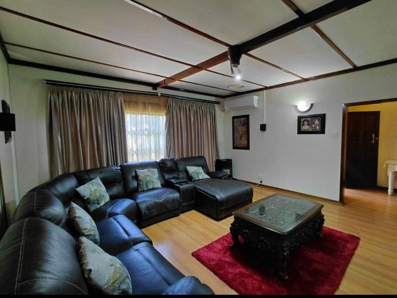 A comfortable living room featuring laminate flooring, a distinctive exposed beam ceiling, and a wall-mounted air conditioning unit.