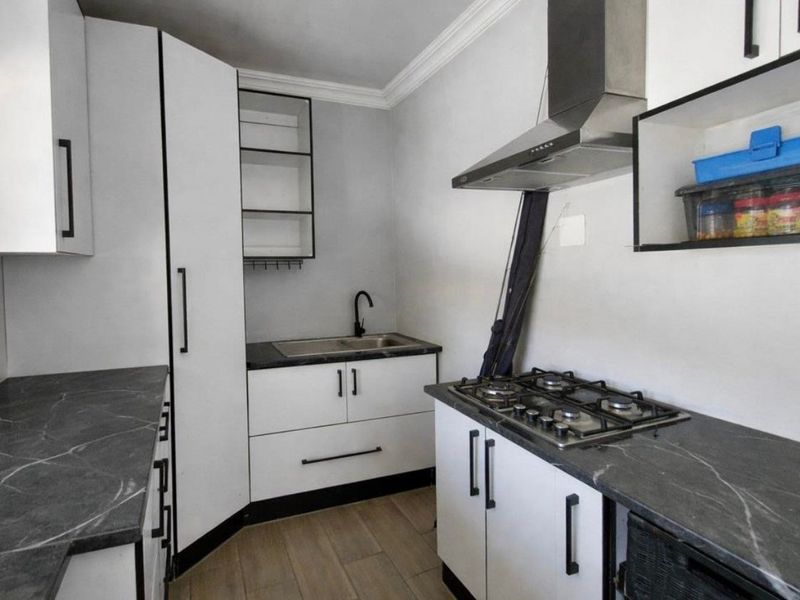 Modern kitchen featuring white cabinetry, dark stone-look countertops, gas hob, extractor fan, and stainless steel sink with contemporary black fixtures.