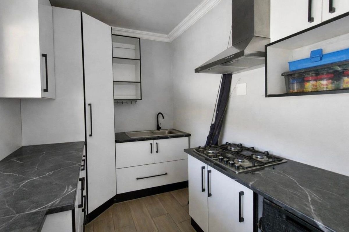 Modern kitchen featuring white cabinetry, dark stone-look countertops, gas hob, extractor fan, and stainless steel sink with contemporary black fixtures.