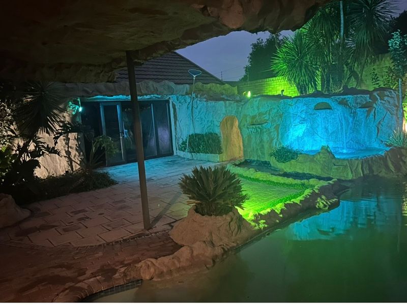 An outdoor pool area featuring a rock-themed water feature, paved patio space, and integrated lighting, creating a unique evening entertainment environment.