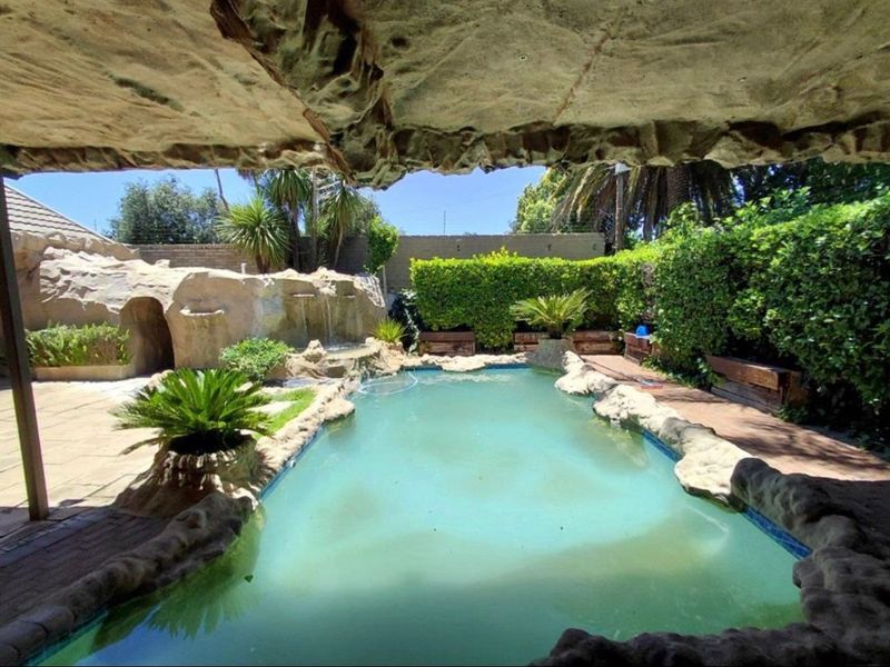 Outdoor pool area featuring a naturalistic rock-style water feature, paved surround, and established garden hedging.