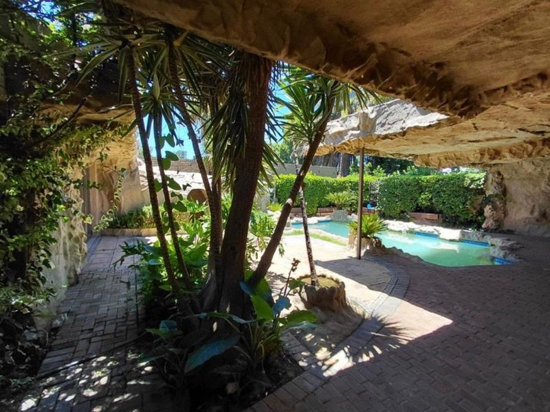 A unique outdoor pool area featuring natural rock formations, paved patio space, and established garden landscaping.
