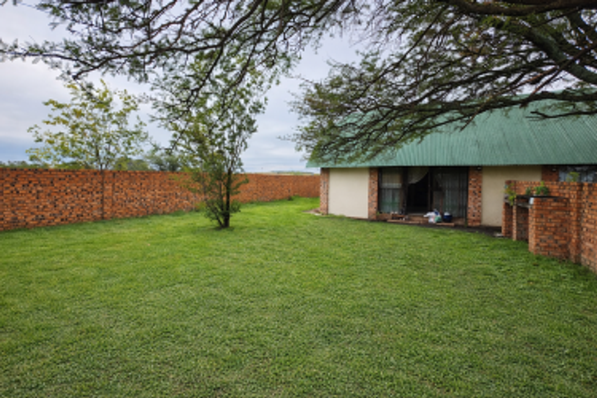 Spacious rear garden featuring a large lawn, brick boundary wall, and a built-in brick braai area adjacent to the main dwelling.