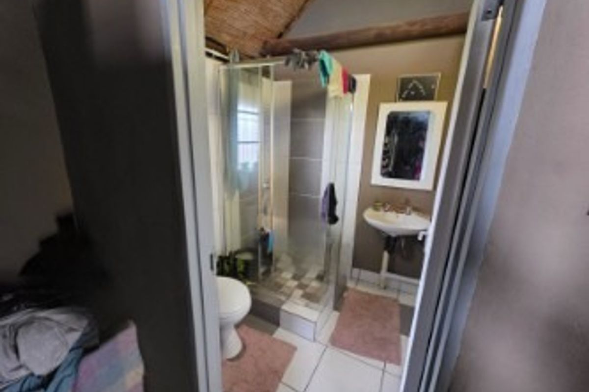 A compact bathroom featuring a shower enclosure, pedestal basin, and exposed timber ceiling beams with tiled flooring.