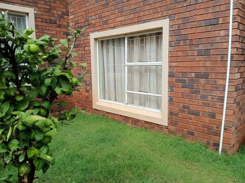 A view of the rear brick facade featuring a sliding window with security bars and a small garden area.