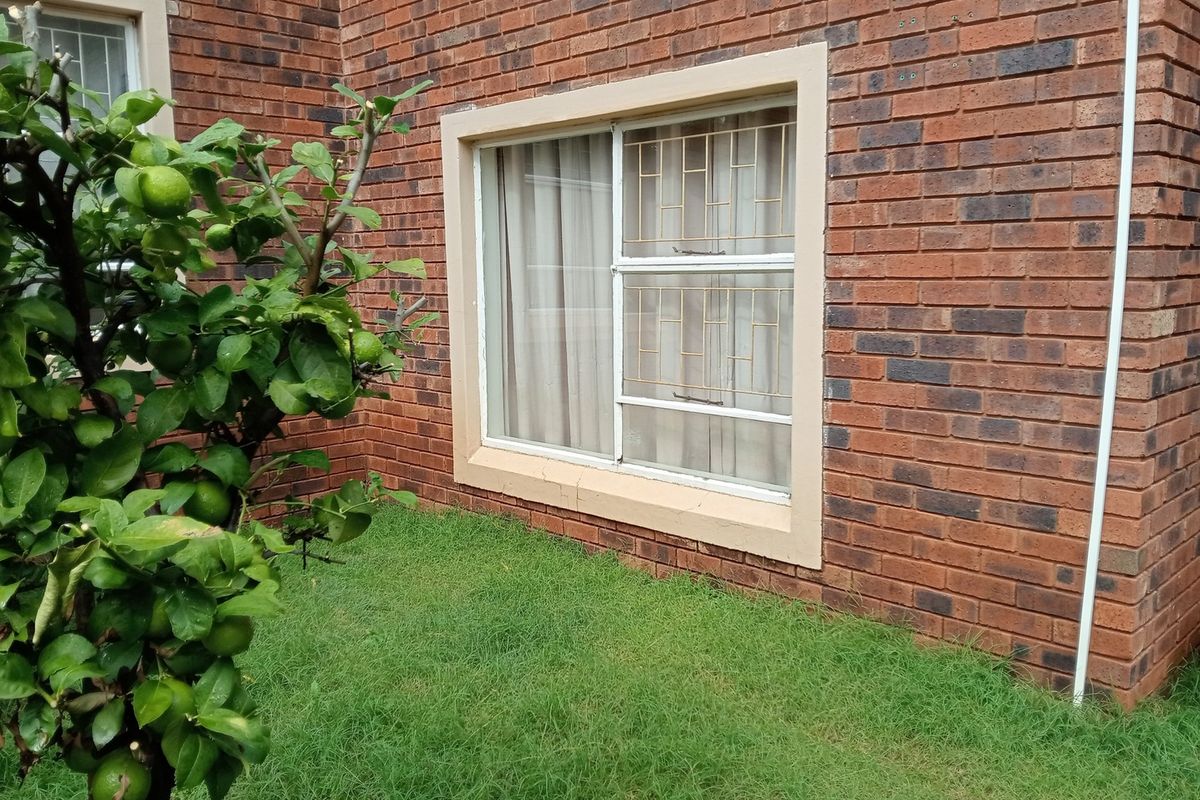 A view of the rear brick facade featuring a sliding window with security bars and a small garden area.