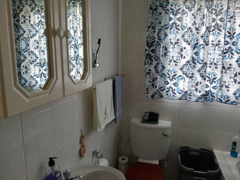 A functional bathroom featuring tiled walls, a pedestal basin, a wall-mounted medicine cabinet, and a standard toilet.