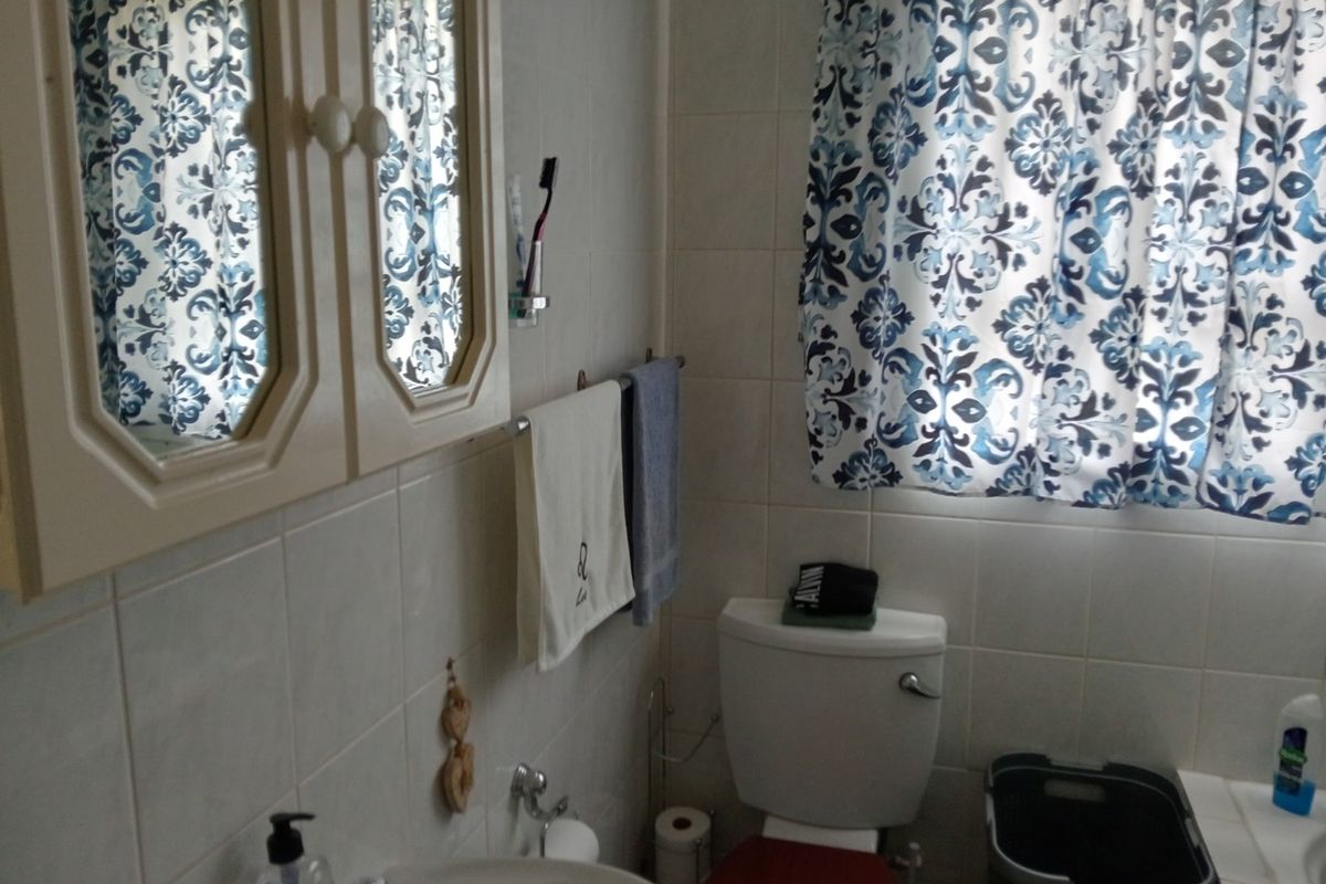 A functional bathroom featuring tiled walls, a pedestal basin, a wall-mounted medicine cabinet, and a standard toilet.
