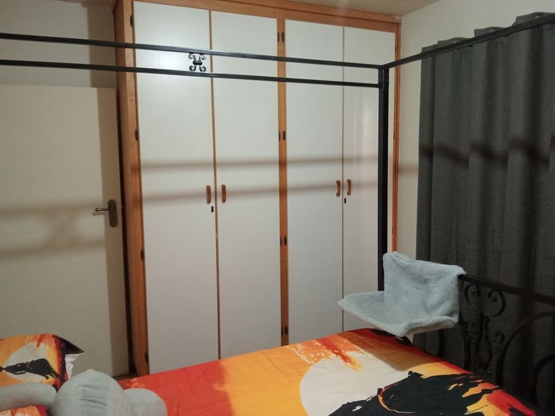 A bedroom featuring a large built-in wardrobe with white doors and wooden trim, providing ample storage space.