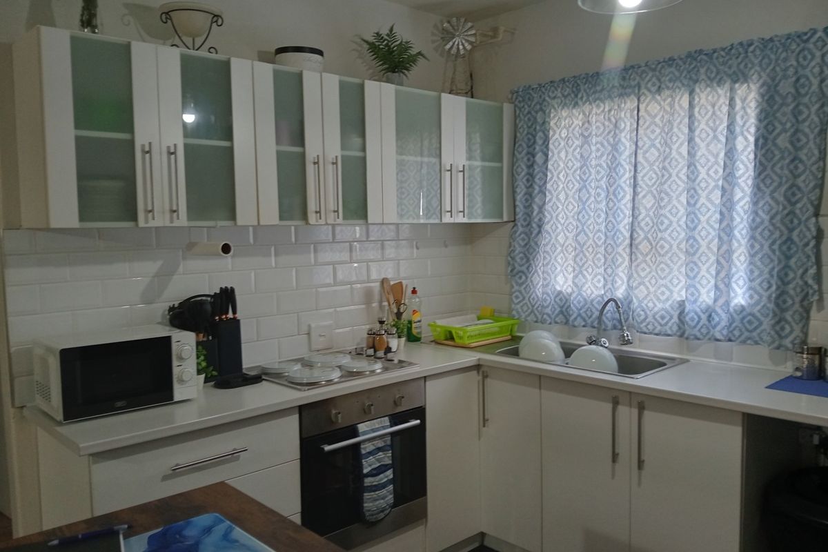 A functional kitchen featuring white cabinetry, subway tile backsplash, integrated stainless steel oven and hob, and a stainless steel sink with a mixer tap.