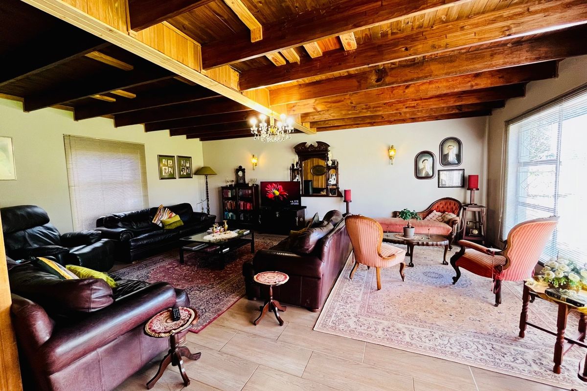 Spacious living room featuring exposed timber ceiling beams, tiled flooring, and classic wall-mounted lighting, creating a warm and traditional atmosphere.