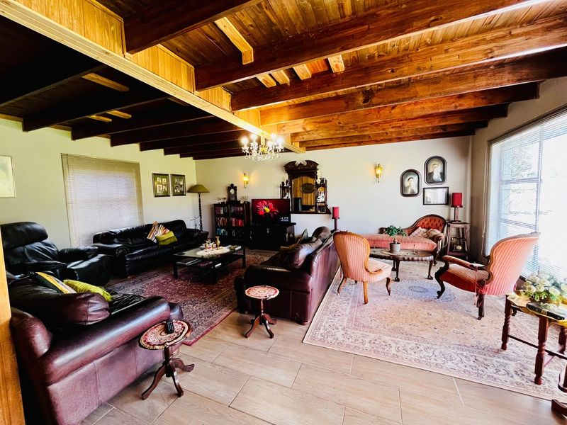 Spacious living room featuring exposed timber ceiling beams, tiled flooring, and classic wall-mounted lighting, creating a warm and traditional atmosphere.