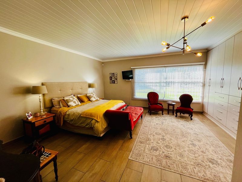 Spacious bedroom featuring tiled flooring, built-in cupboards, a tongue and groove ceiling, and a modern chandelier, offering a comfortable and well-maintained living space.