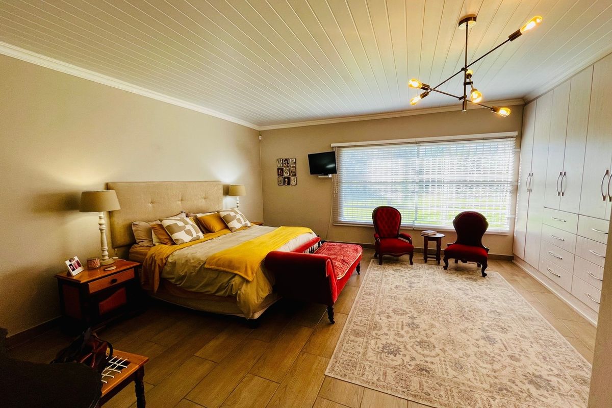 Spacious bedroom featuring tiled flooring, built-in cupboards, a tongue and groove ceiling, and a modern chandelier, offering a comfortable and well-maintained living space.