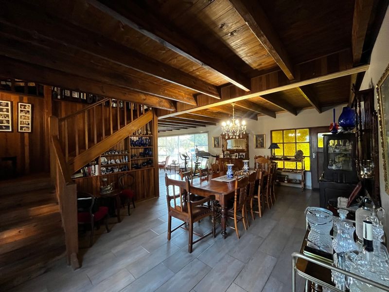 Spacious dining area featuring exposed timber ceiling beams, a classic timber staircase, built-in shelving, and large windows allowing for natural light.