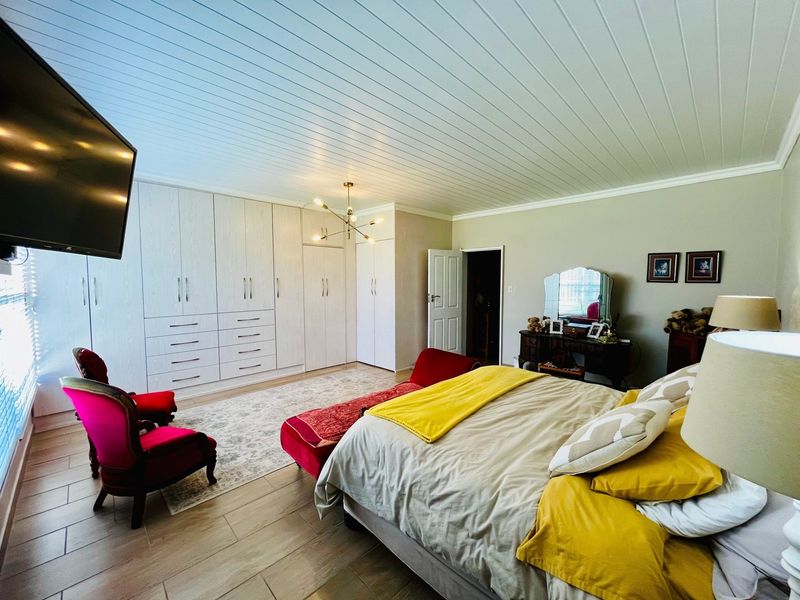 Spacious bedroom featuring extensive built-in cabinetry, light-toned tiled flooring, and a distinctive tongue and groove ceiling with a contemporary light fixture.