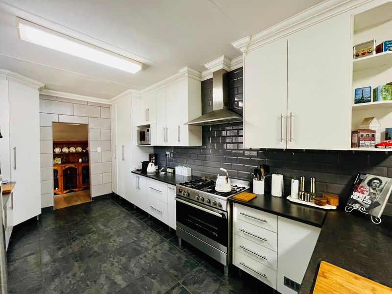 Modern kitchen featuring white cabinetry, dark stone countertops, a gas stove with stainless steel extractor fan, and a stylish dark subway tile backsplash.