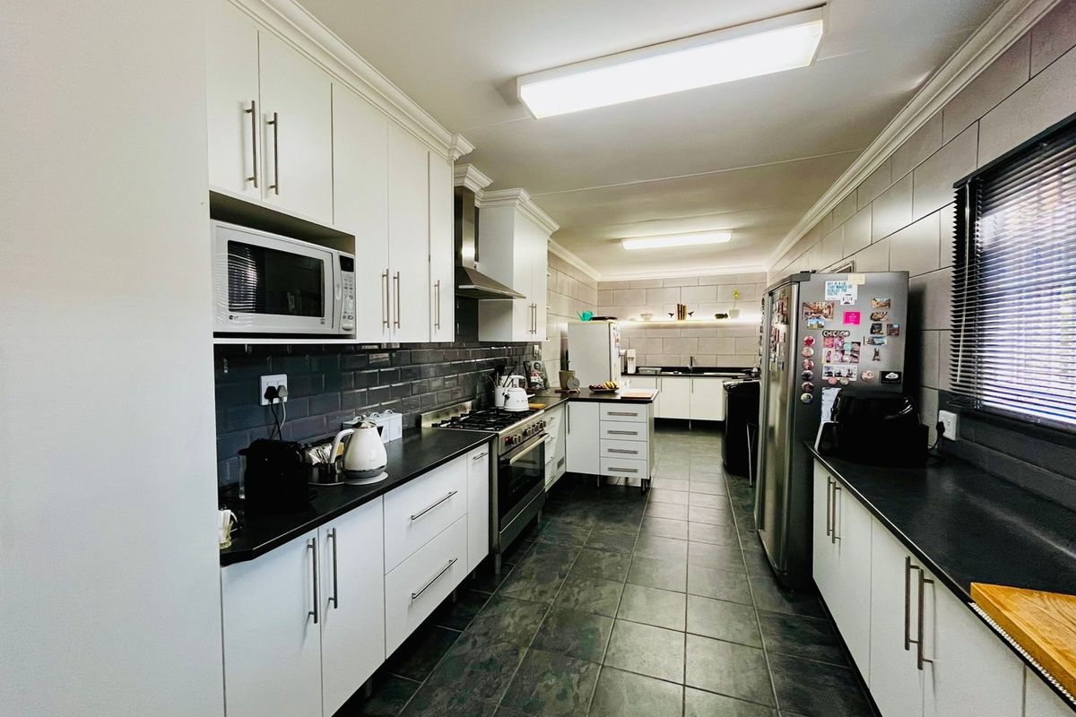 A well-appointed galley-style kitchen featuring modern white cabinetry, dark countertops, a gas hob, integrated oven, and sleek tiled finishes throughout.