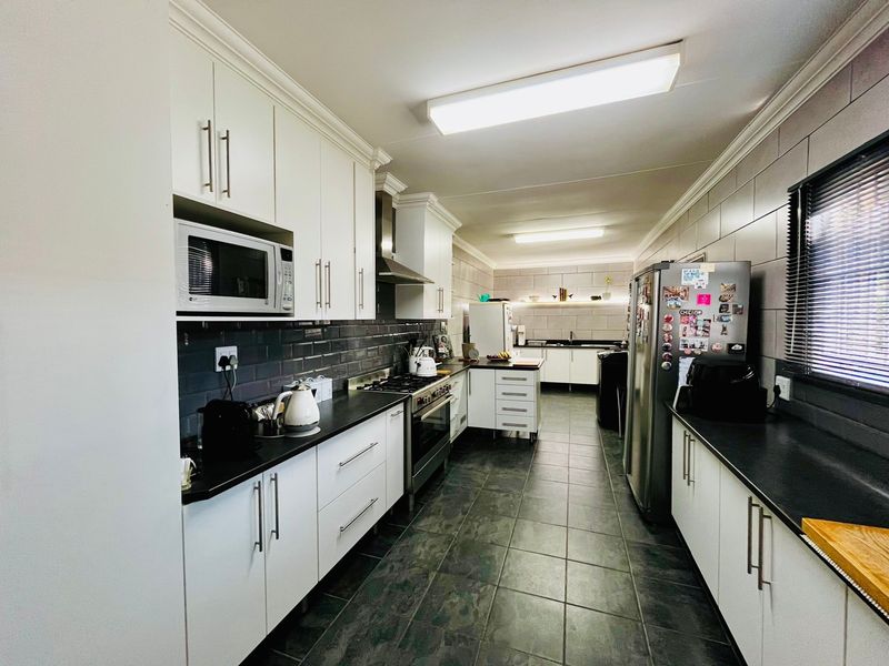 A well-appointed galley-style kitchen featuring modern white cabinetry, dark countertops, a gas hob, integrated oven, and sleek tiled finishes throughout.