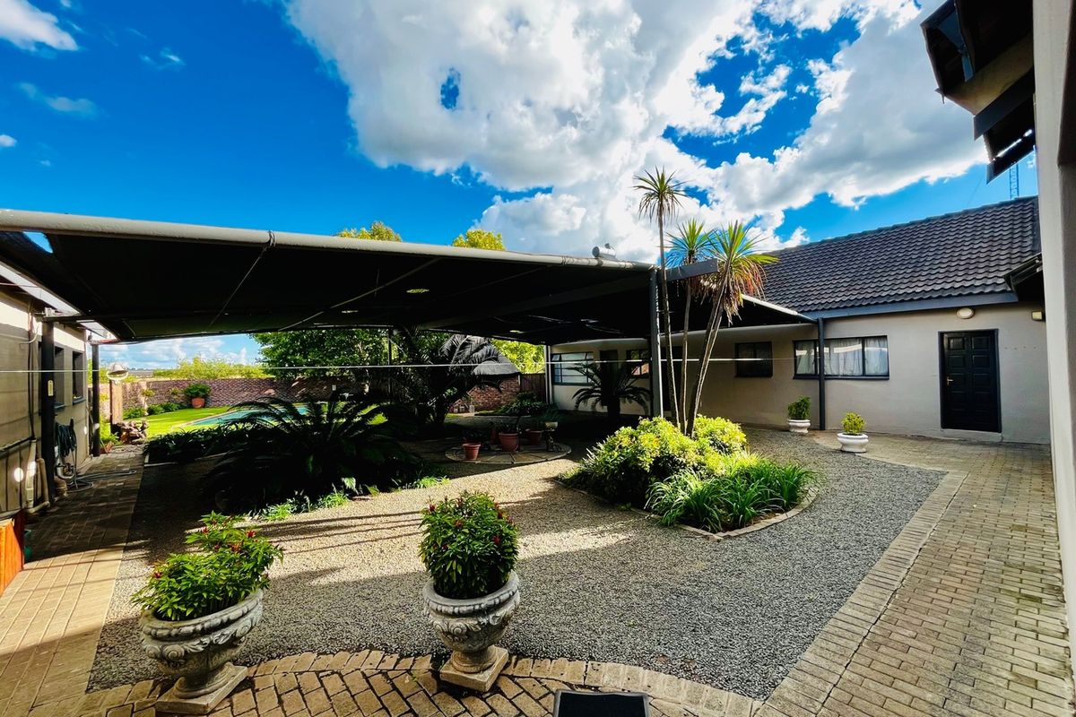 A well-maintained rear courtyard featuring a large shade sail, paved walkways, and landscaped garden beds, providing a functional outdoor entertainment area.
