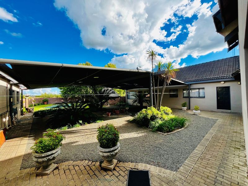 A well-maintained rear courtyard featuring a large shade sail, paved walkways, and landscaped garden beds, providing a functional outdoor entertainment area.