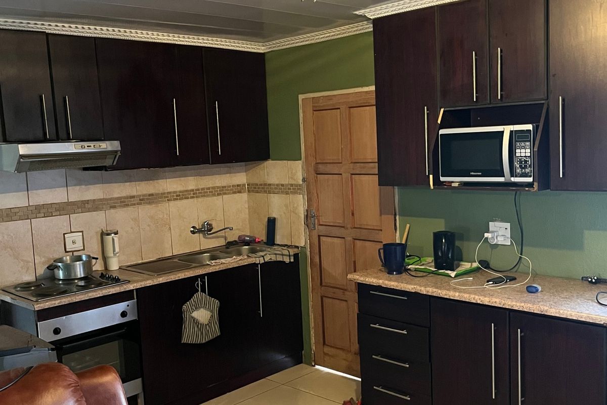 A functional kitchen featuring dark wood cabinetry, laminate countertops, built-in appliances, and tiled flooring with a neutral backsplash.