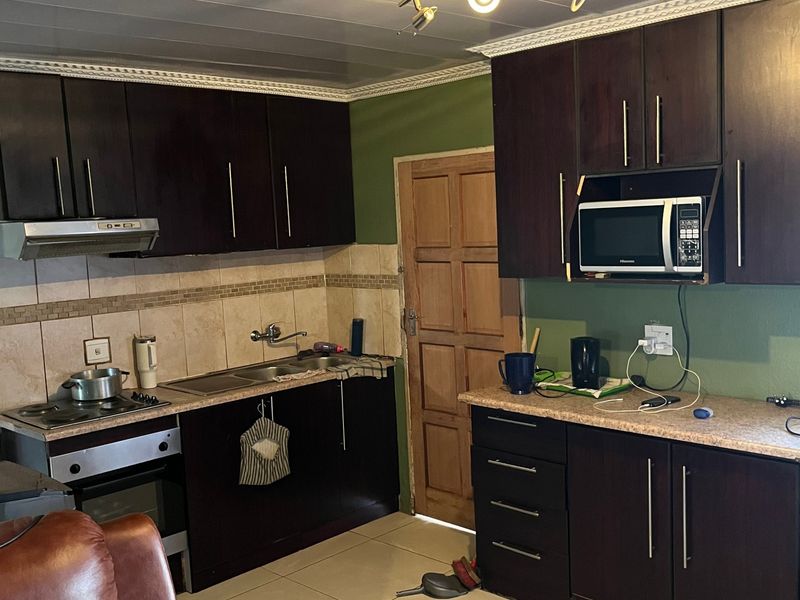 A functional kitchen featuring dark wood cabinetry, laminate countertops, built-in appliances, and tiled flooring with a neutral backsplash.