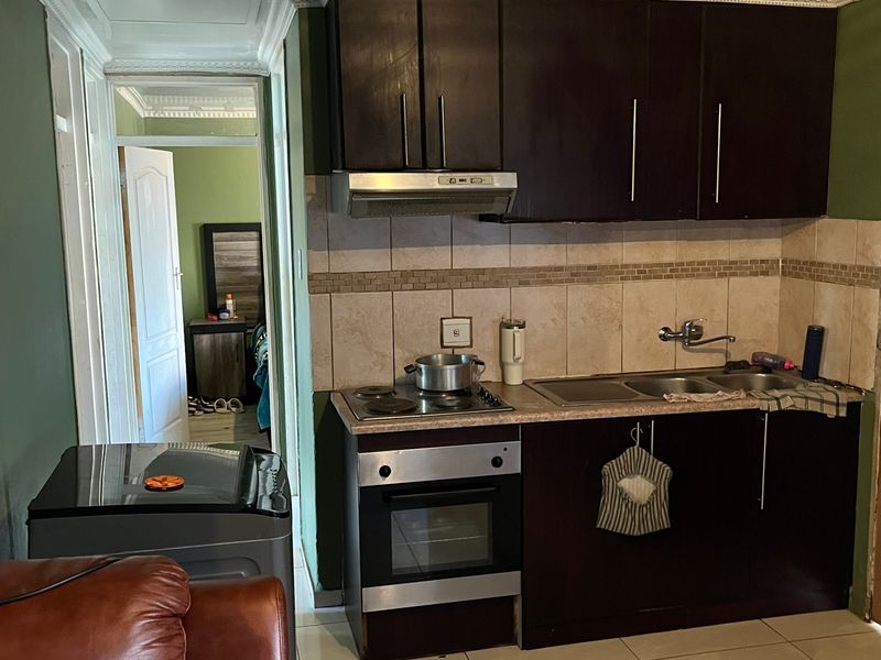 Compact kitchen featuring dark built-in cabinetry, integrated oven and hob, tiled backsplash, and neutral floor tiles, providing a functional cooking space.