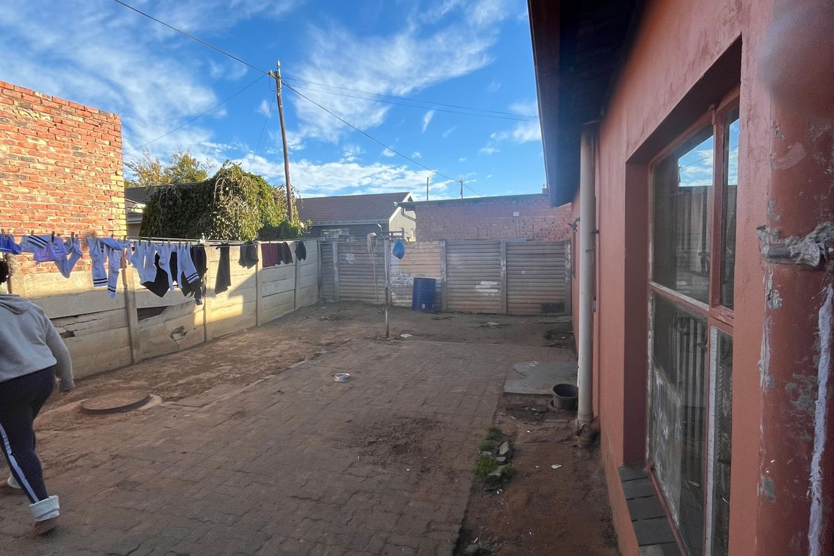 Rear exterior area featuring a paved courtyard, enclosed by precast and brick boundary walls, showing signs of wear and maintenance requirements.