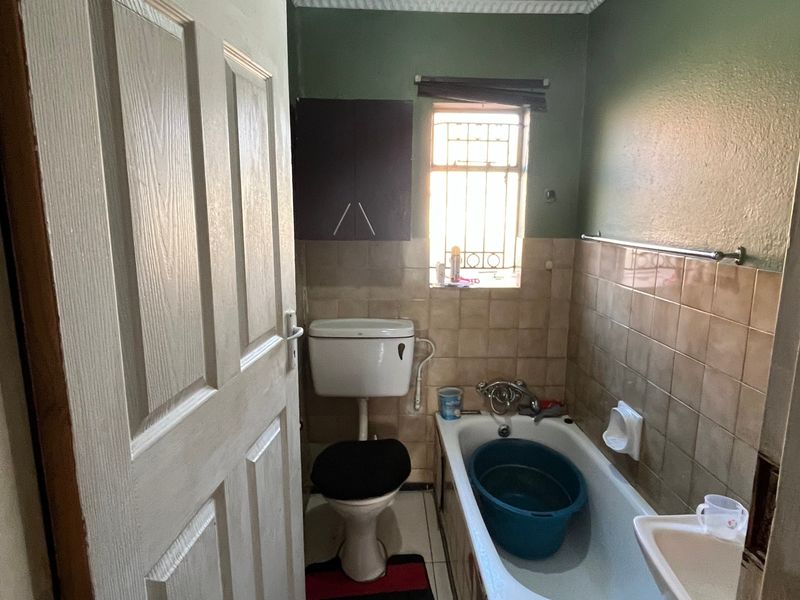 A compact bathroom featuring a bathtub, toilet, and wall-mounted storage, requiring cosmetic updates to modernize the dated finishes.