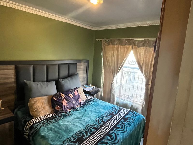 A bedroom featuring green walls, decorative ceiling cornicing, and a window fitted with a security gate.