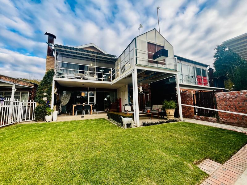 Rear view of the property featuring a landscaped lawn, a covered ground-floor patio, and an upper-level balcony with a chimney.