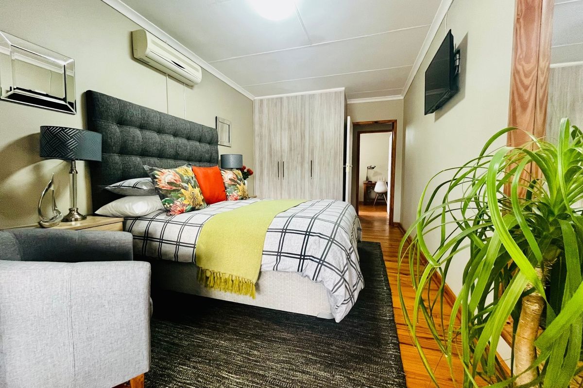 A well-maintained bedroom featuring timber flooring, a built-in wardrobe, and a wall-mounted air conditioning unit.