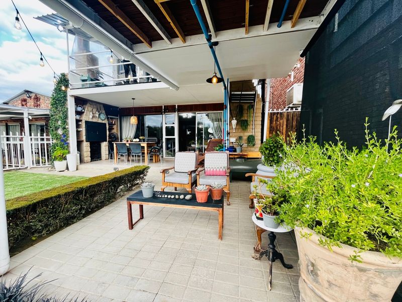 A spacious covered patio area featuring paved flooring, exposed timber ceiling beams, and a built-in stone fireplace, ideal for outdoor entertaining.