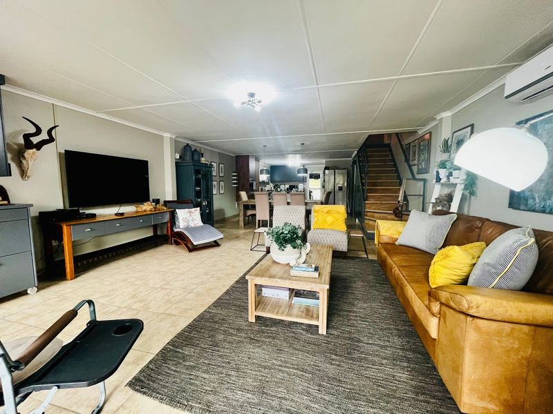 Spacious open-plan living and dining area featuring tiled flooring, a central staircase, and integrated air conditioning, creating a functional and connected family space.