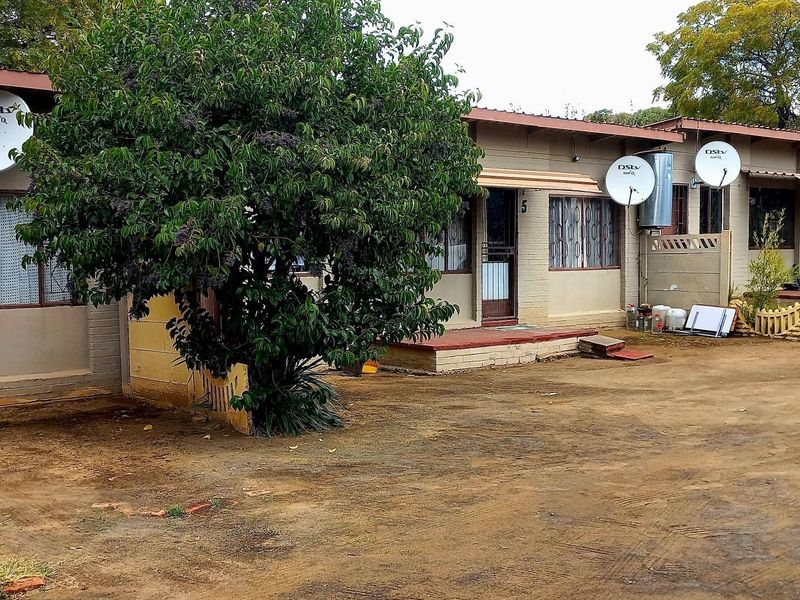 Front view of a cluster property featuring a brick facade, security gates, and multiple satellite dishes, with an unpaved driveway area.