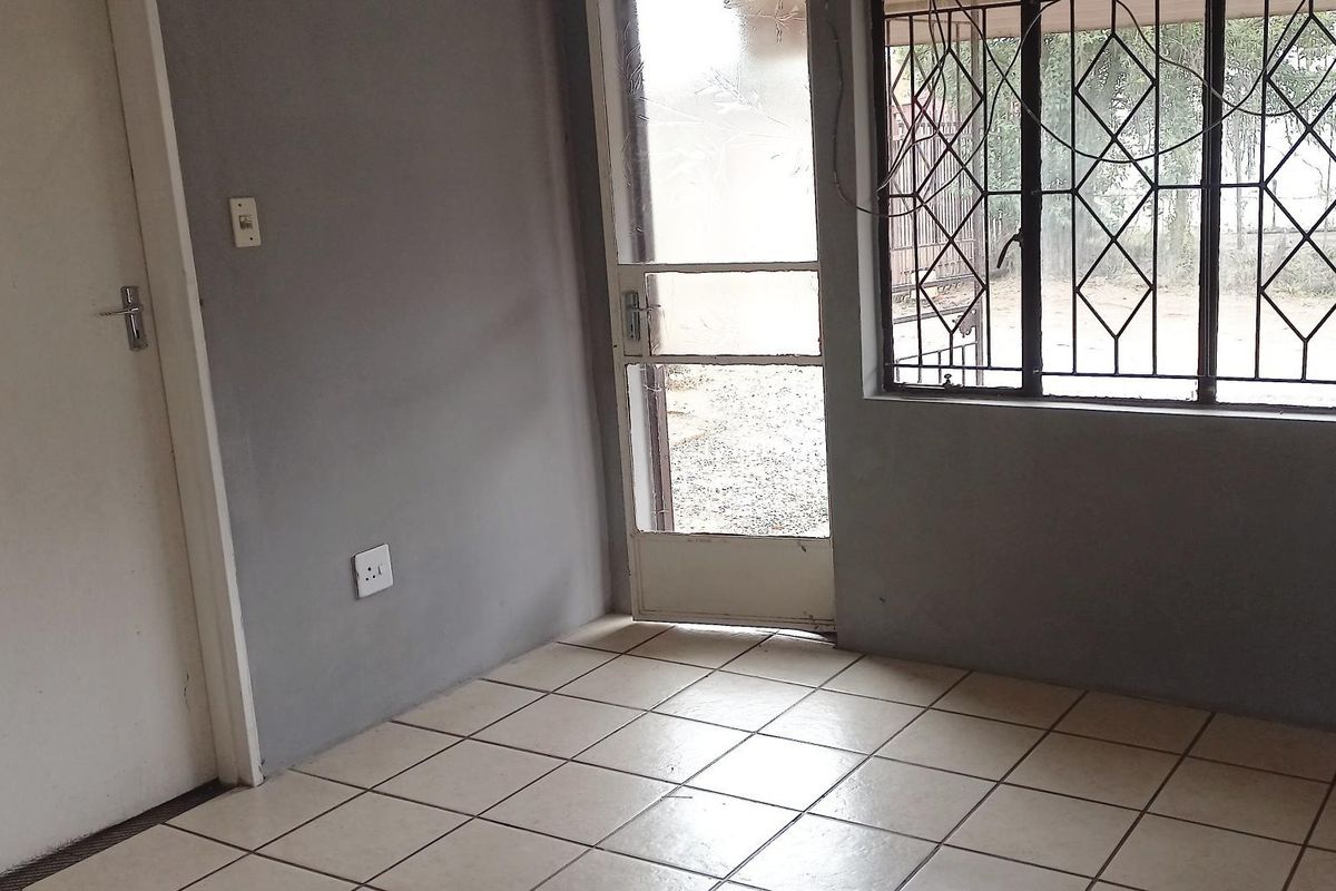 An empty living area featuring tiled flooring, a security gate, and burglar bars on the windows, providing a blank canvas for interior updates.